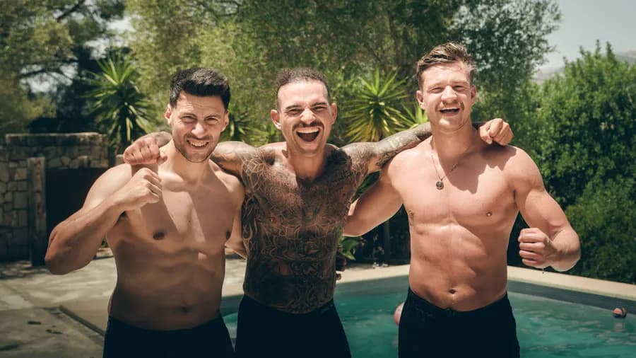Vier Männer stehen lachend Arm in Arm am Pool.