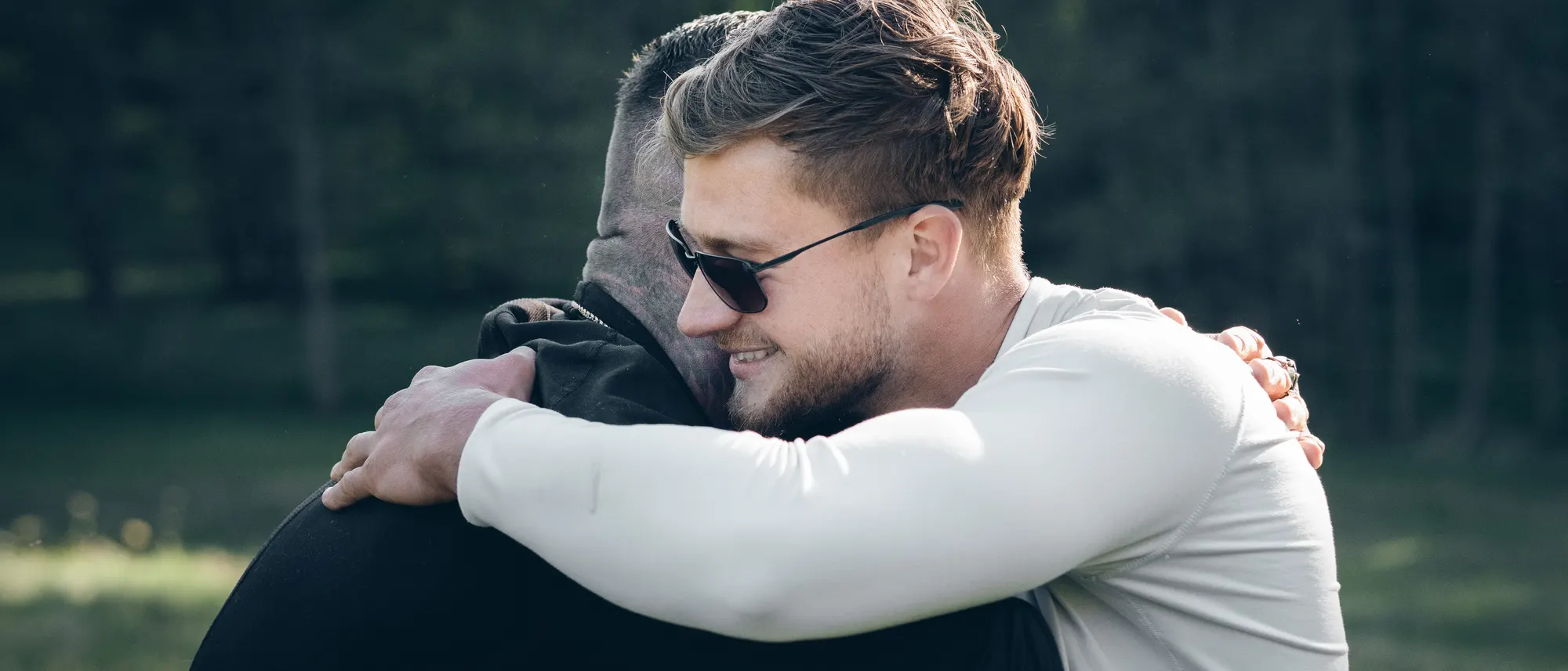 Jurij und Timo umarmen sich lachend auf einer Waldlichtung.