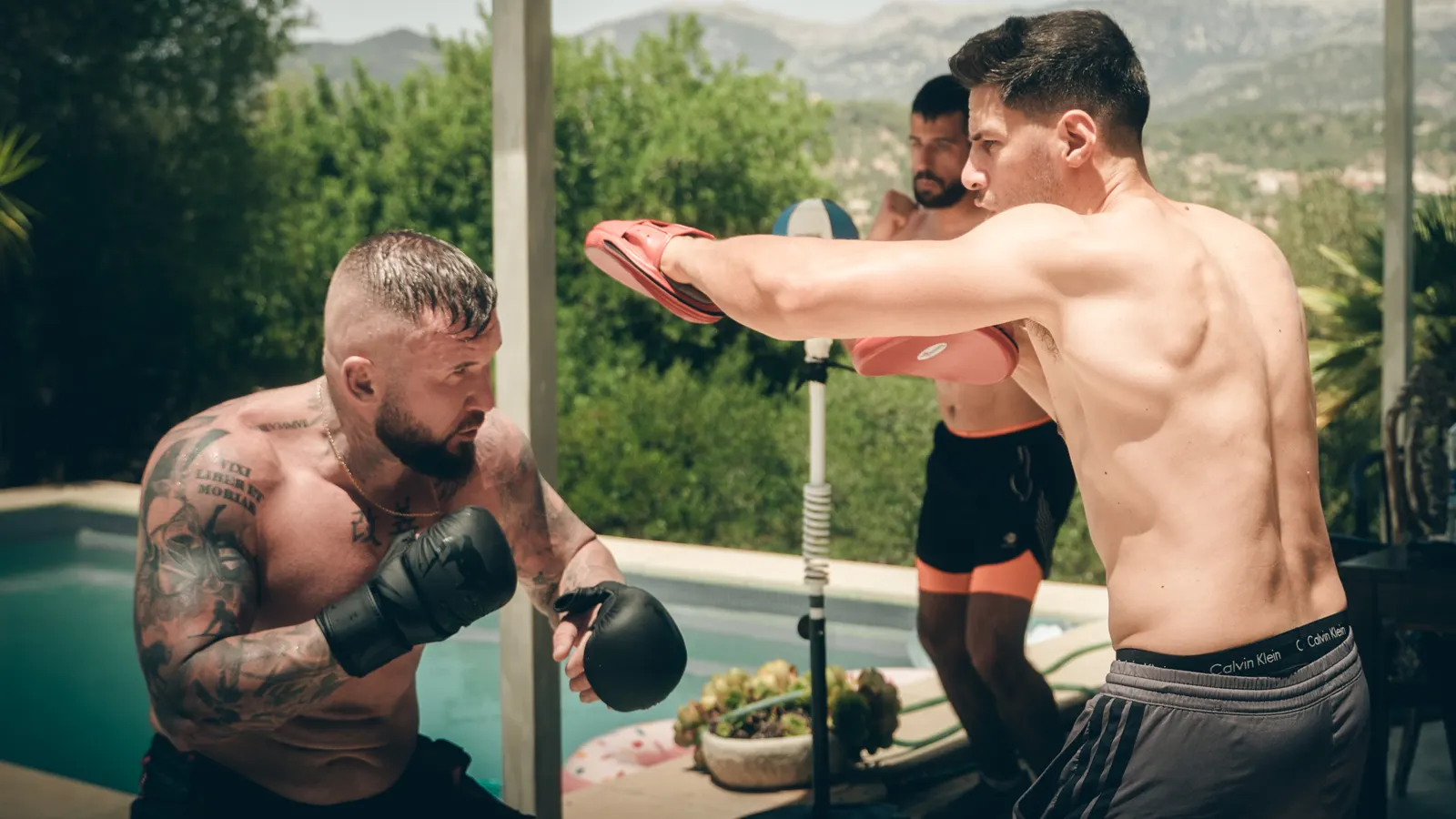 Ein Mann hält am Pool die Pratzen, ein anderer schlägt mit Boxhandschuhen darauf.